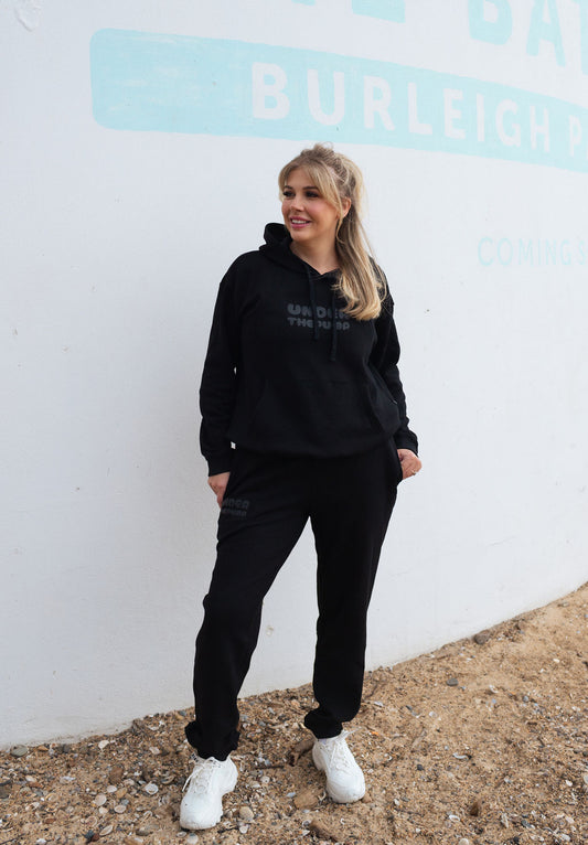 Black breastfeeding-friendly tracksuit with hidden zips, unzipped for easy nursing access, showing a mom comfortably feeding her baby. Super soft fabric, stylish and practical design for nursing mothers.